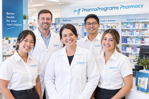 A smiling community pharmacy team standing in front of the dispensary shelves
